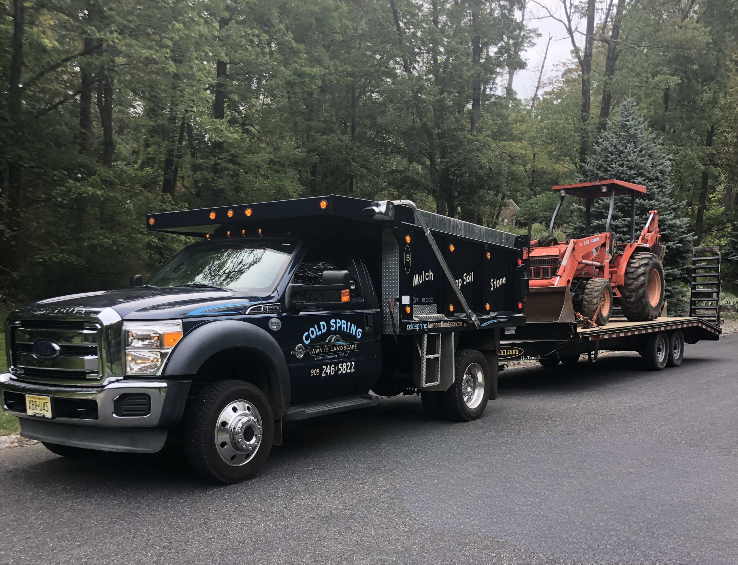 landscaping services - Cold Spring Lawn & Landscape - truct with logo on the side, pulling a flatbed trailer with a tractor on it
